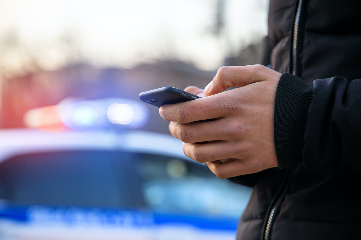 Man holding cell phone with police car in street